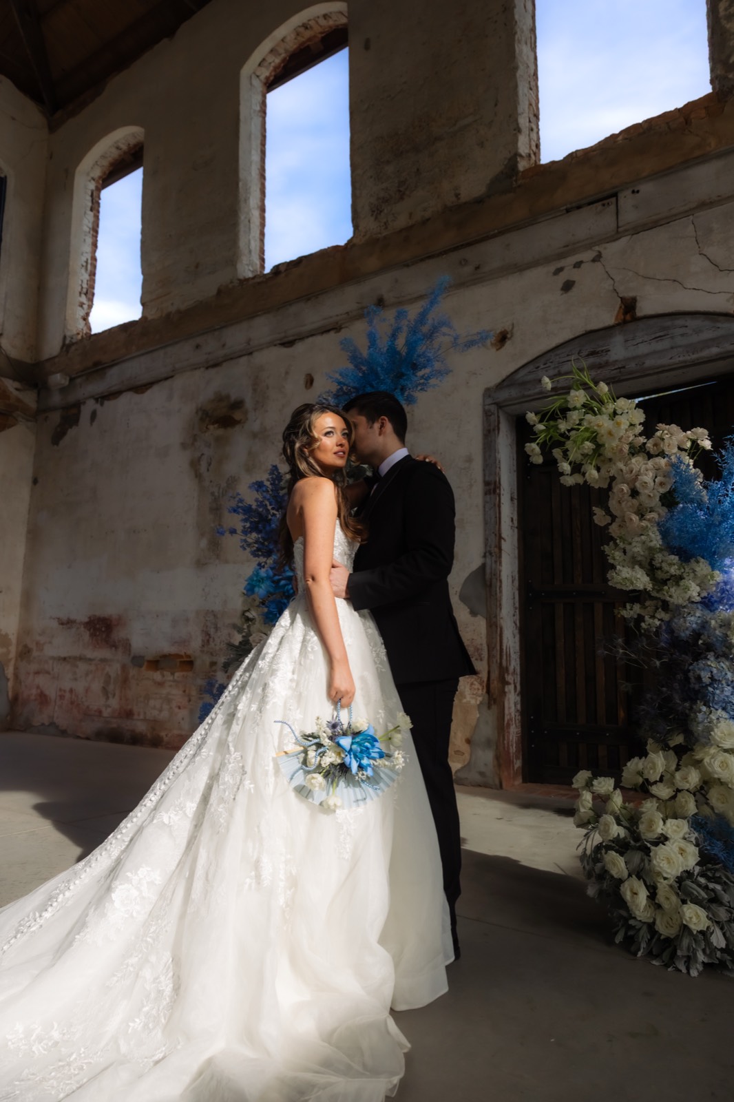 Bride and groom kissing in a ruined venue ceremony setup with blue florals