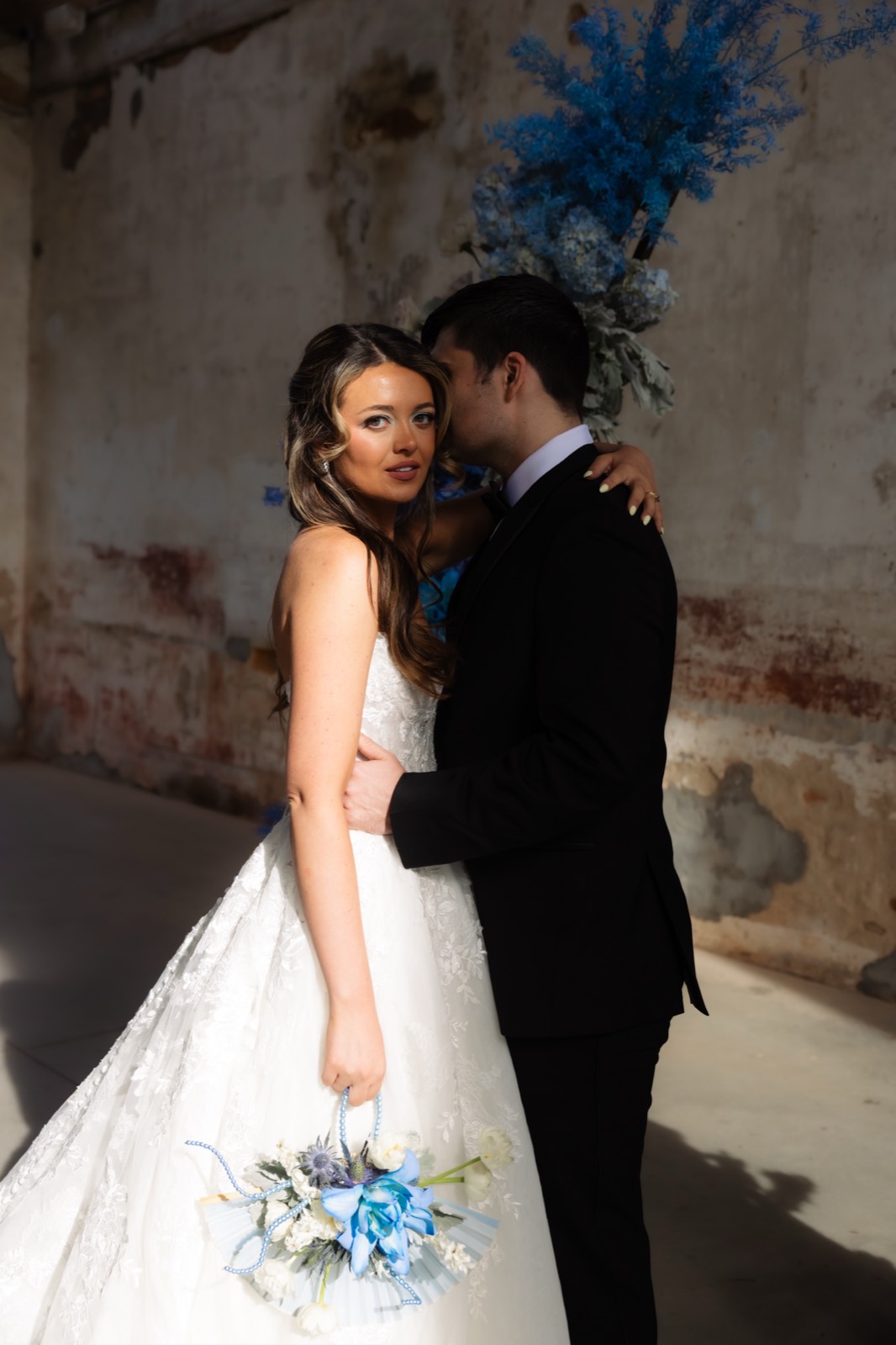 Bride holding bouquet with groom behind her beside blue floral installations