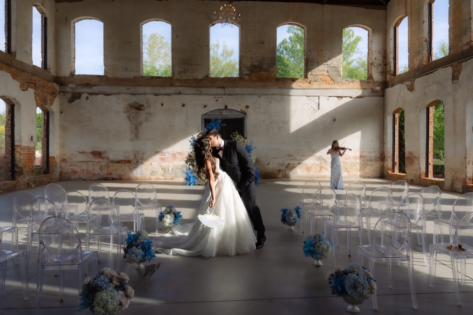 Wide ceremony editorial with bride and groom kissing while violinist performs